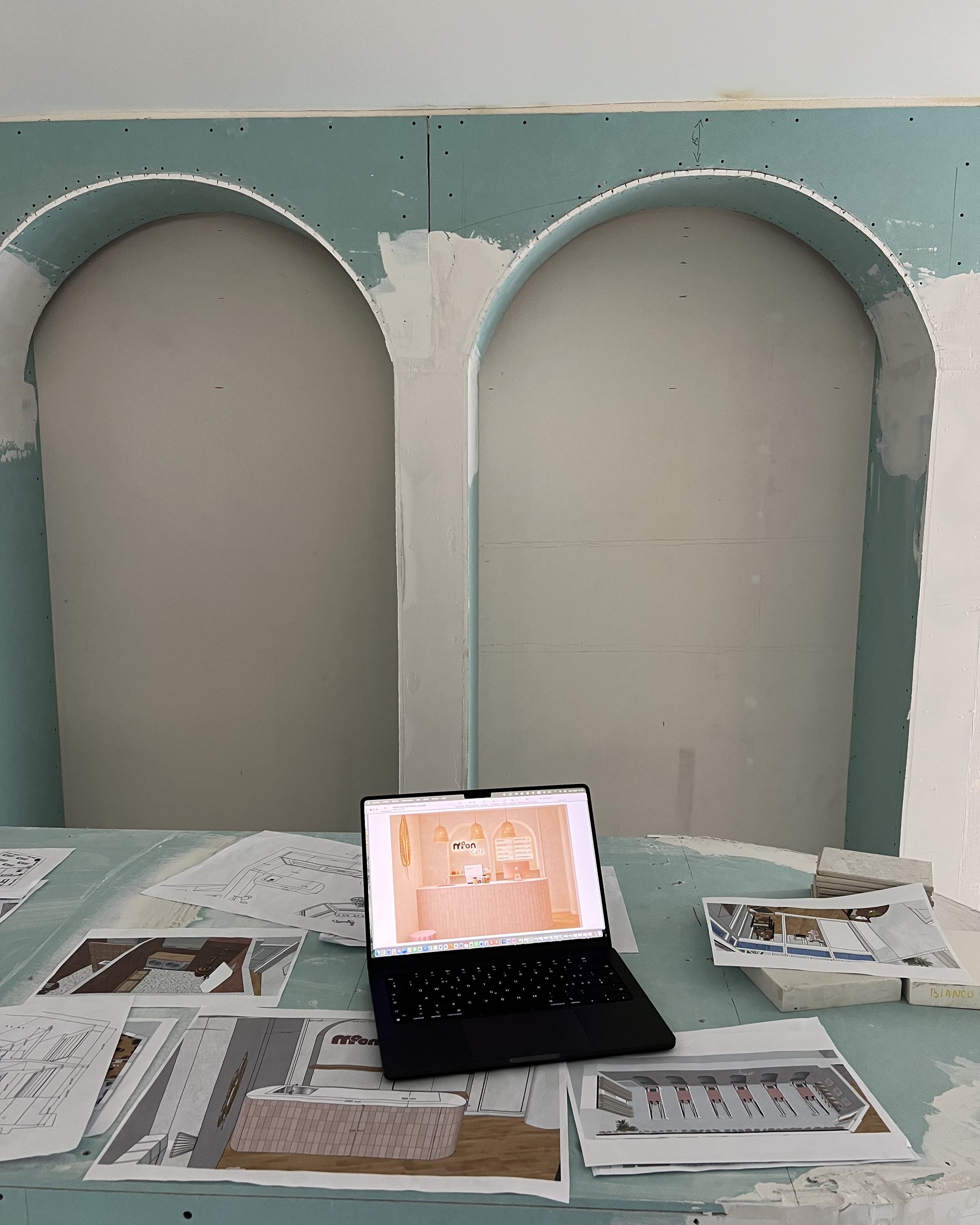 Two unfinished plasterboard arches on site with plans and a laptop in front