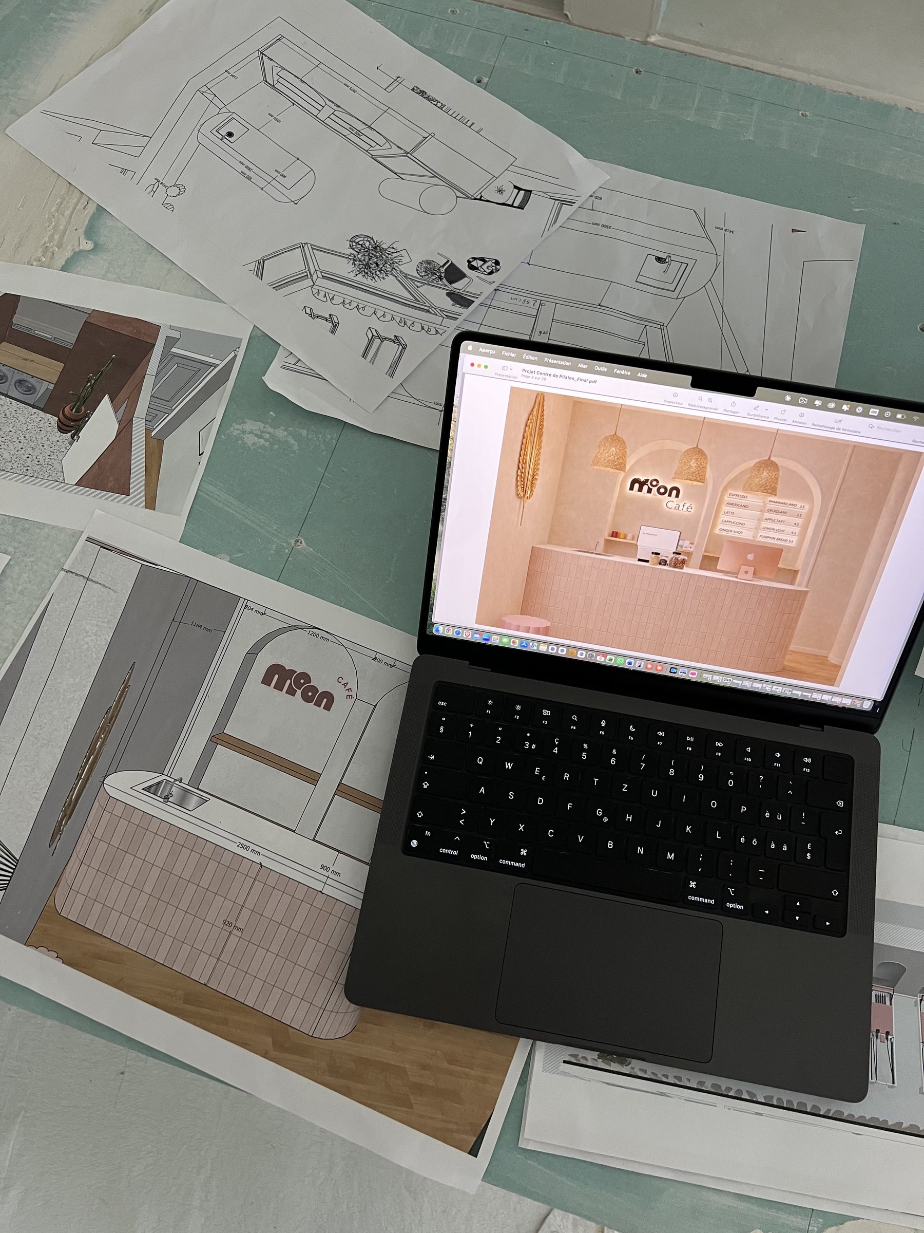 Laptop showing the café render next to printed plans on the unfinished bar