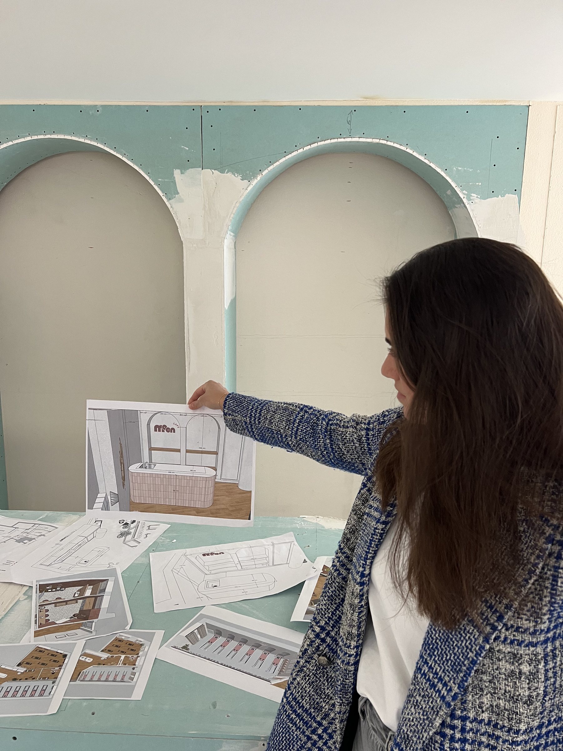 Alessia Di Dio holding the 3D render of the café in front of the unfinished plasterboard arches