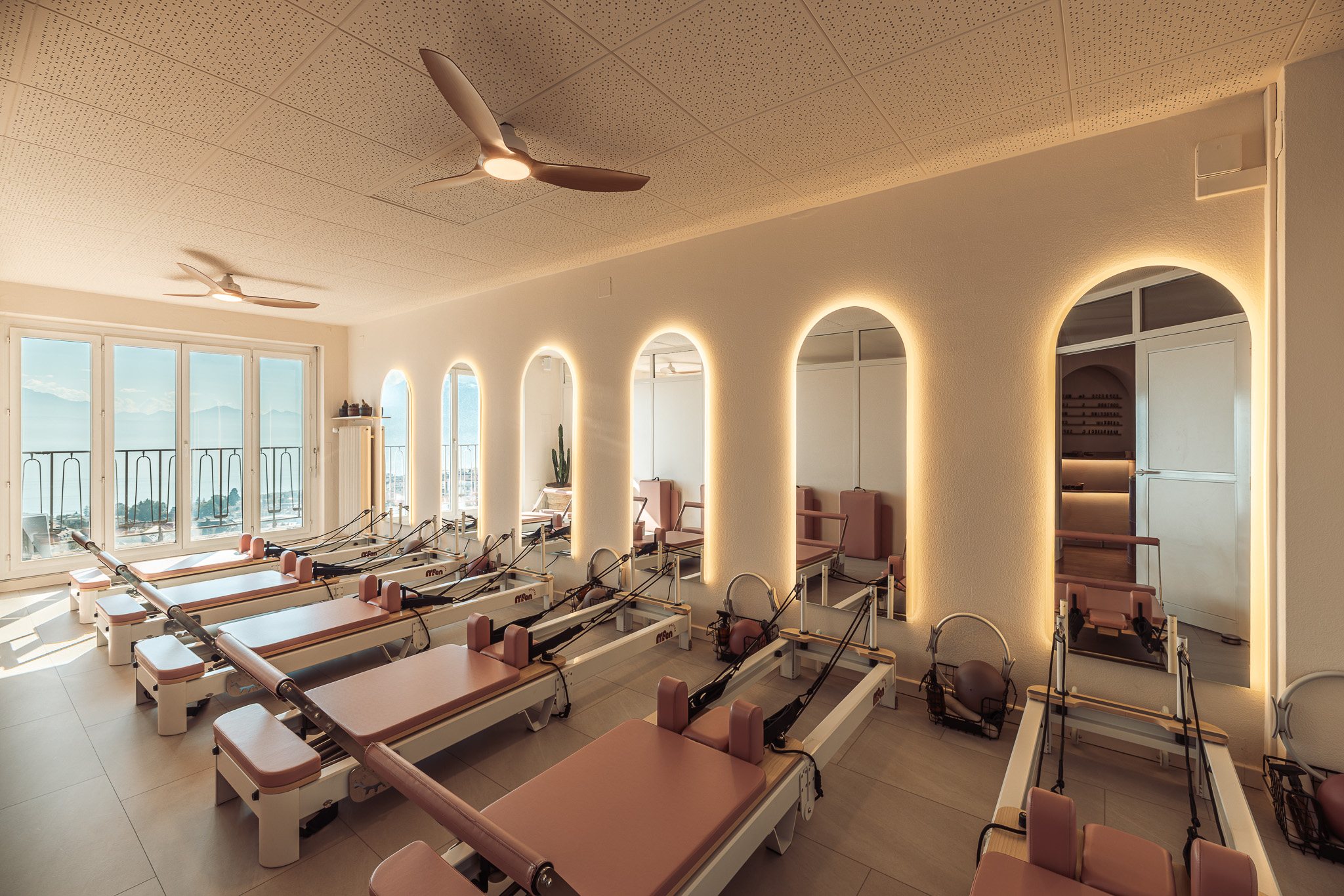 Wide view of the reformer studio with a row of reformers and backlit arched mirrors