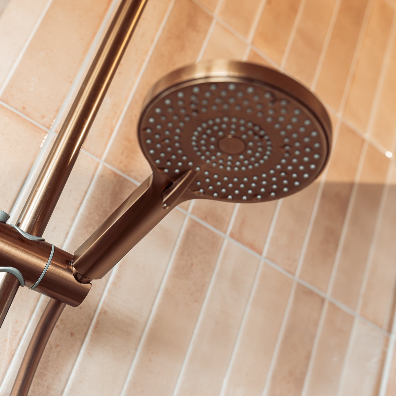 Copper shower head against sand-coloured tiles